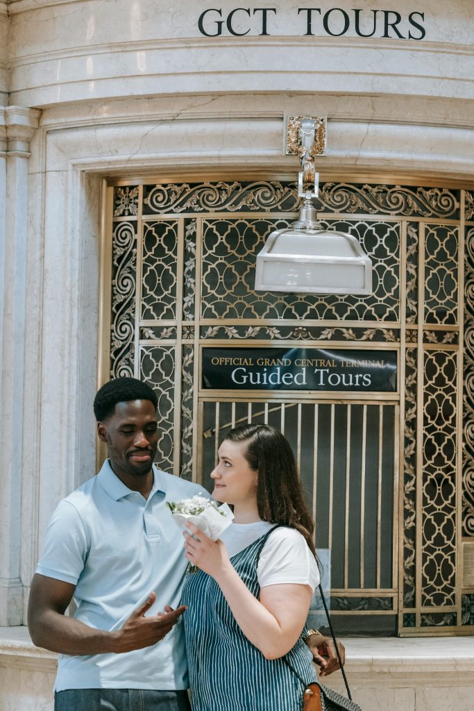Happy couple standing outside a guided tour office at Grand Central Terminal, sharing a moment.